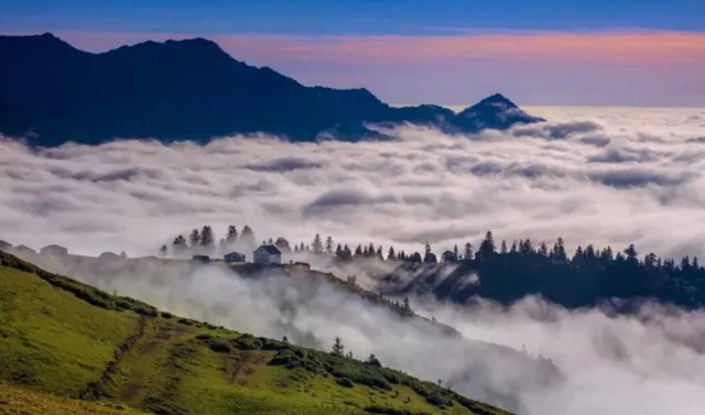 Wooden cabins on the slope of Gomis Mta with mist in the forest below
